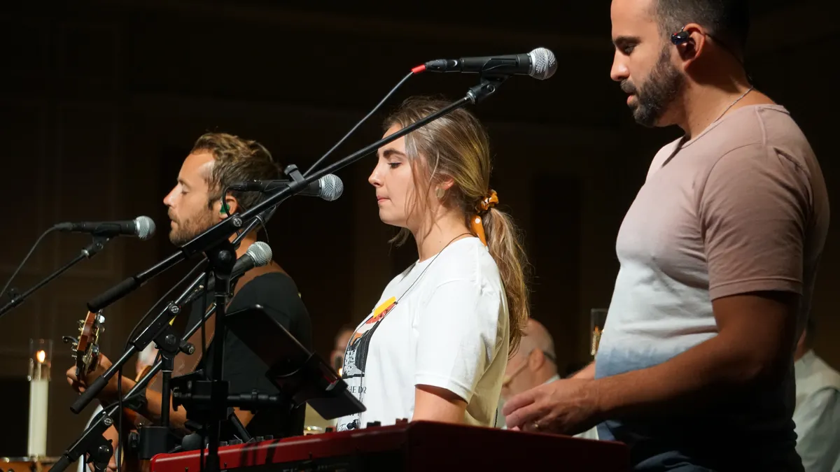 Three musicians sing and play onstage at a Steubenville conference