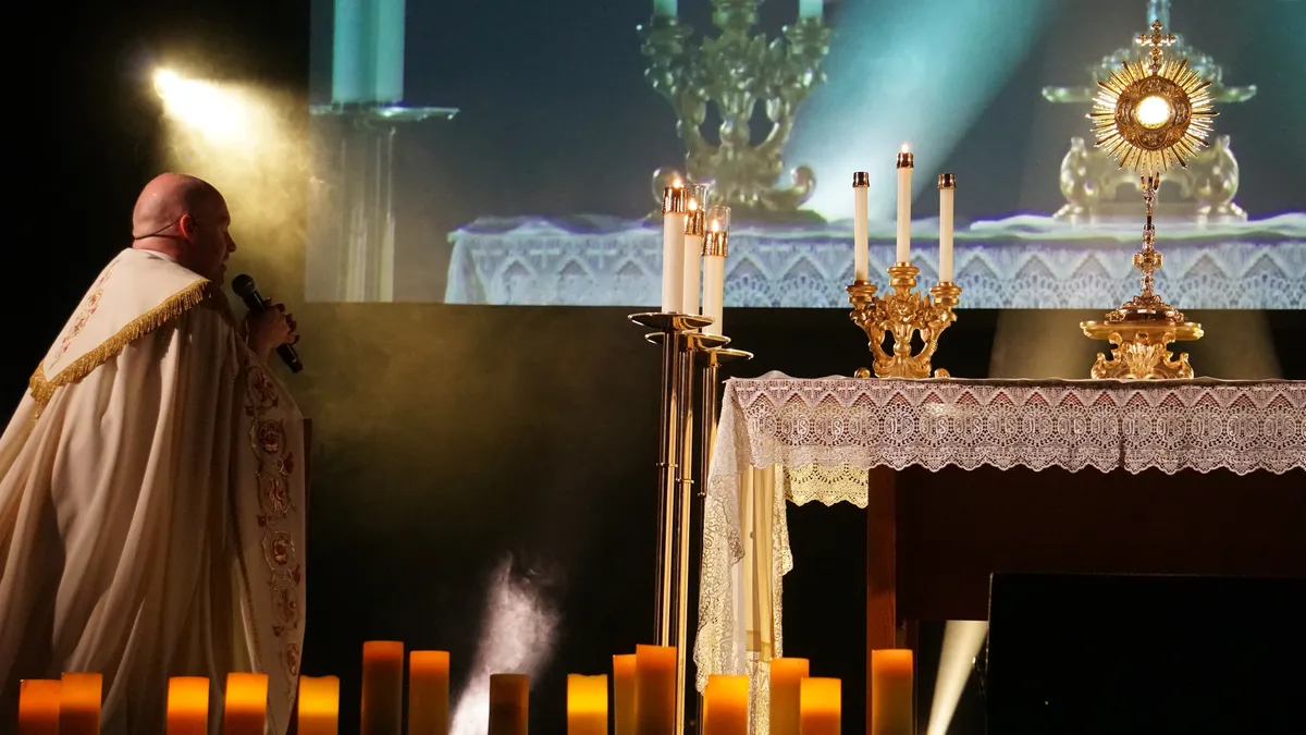 A priest kneels before an illuminated altar during Eucharistic adoration