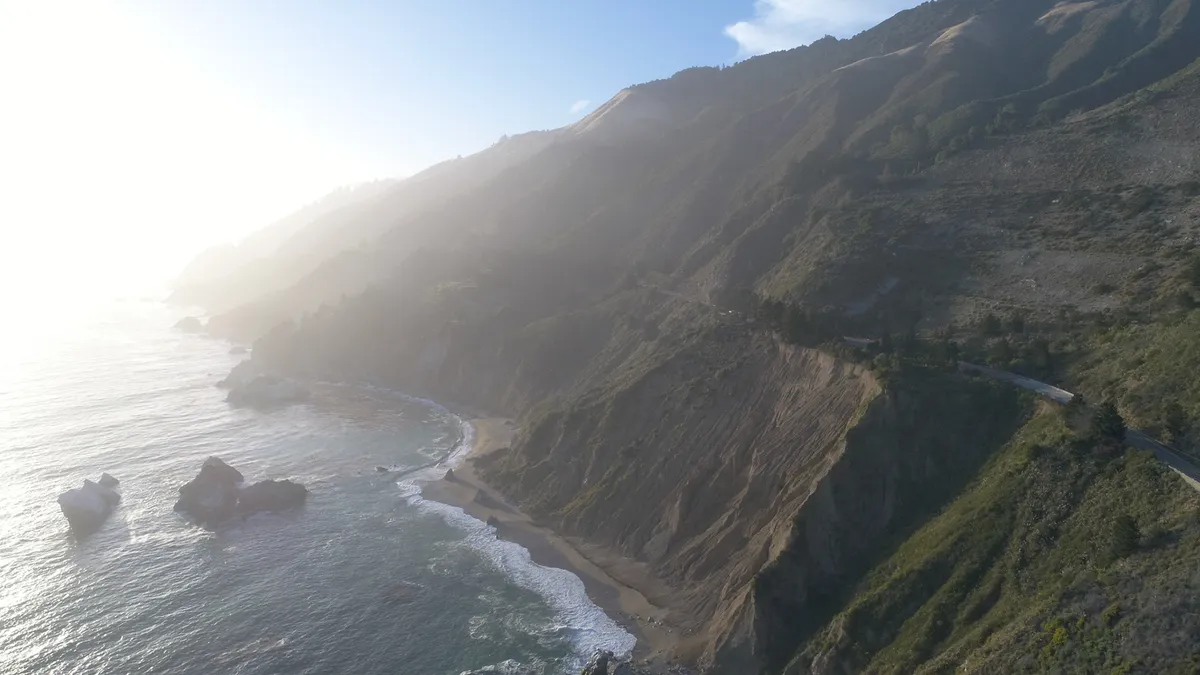 A coastal highway curves between sunlit mountains and the ocean