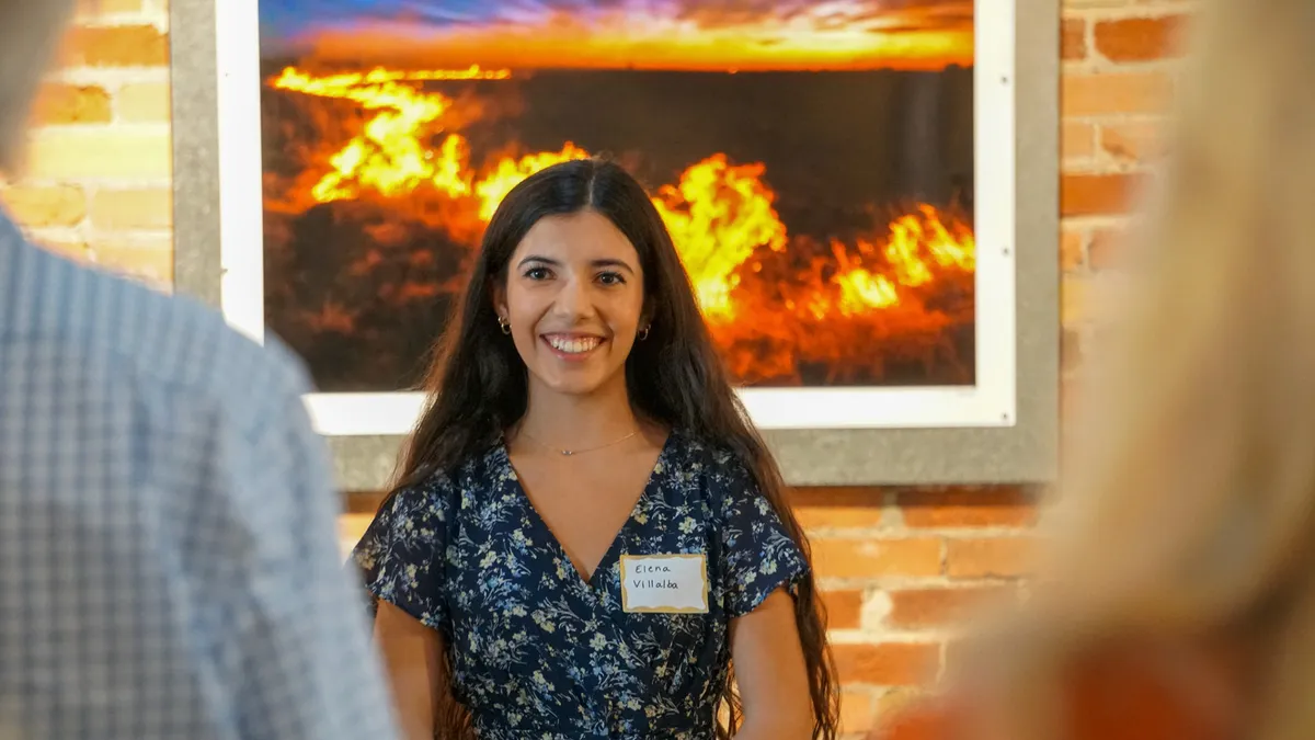 A smiling attendee stands in front of a framed landscape photograph