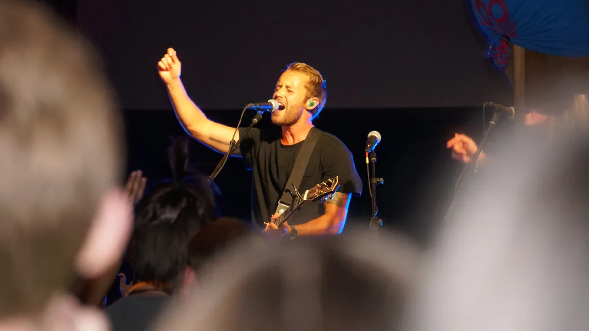 A worship leader sings and raises one hand onstage