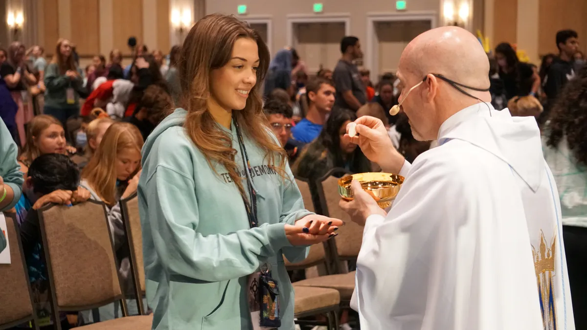 A priest distributes Communion to a conference attendee