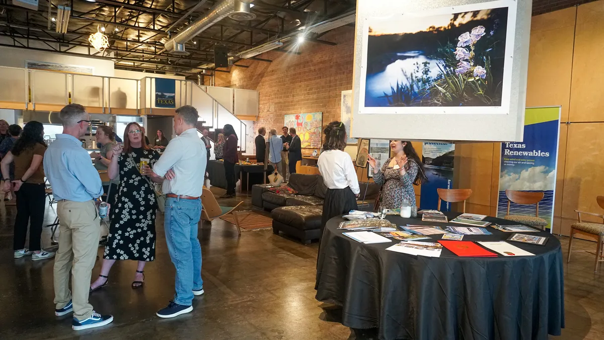 Guests talk beside environmental displays and a framed wildflower photograph in a brick-walled event space