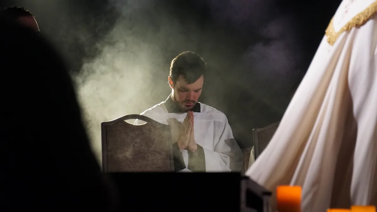 A priest bows his head in prayer as incense rises