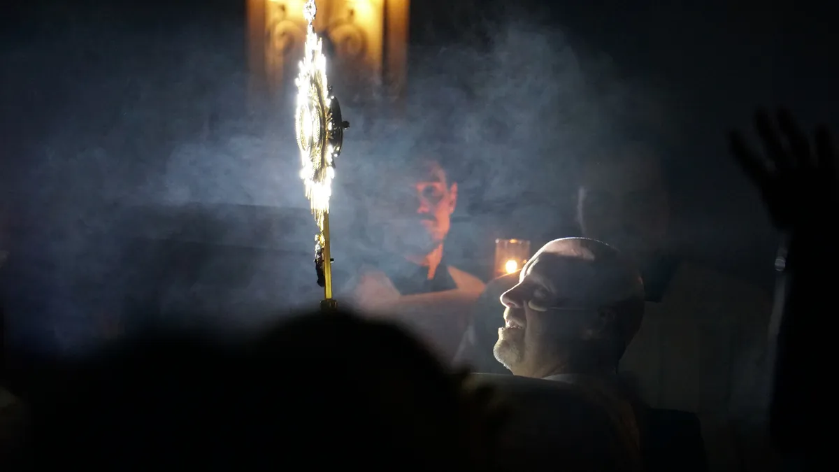 A priest raises a monstrance through a cloud of incense